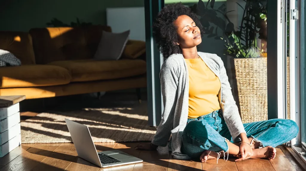 image of a woman sitting in the sunlight with a laptop next to her showing Work-Life Balance During The Holidays