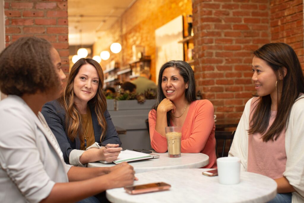 Four women share in a meaningful conversation as they sit together around a table. The camaraderie is evident creating a warm and harmonious scene showing the effects of 5 Tips for Effective Communication.