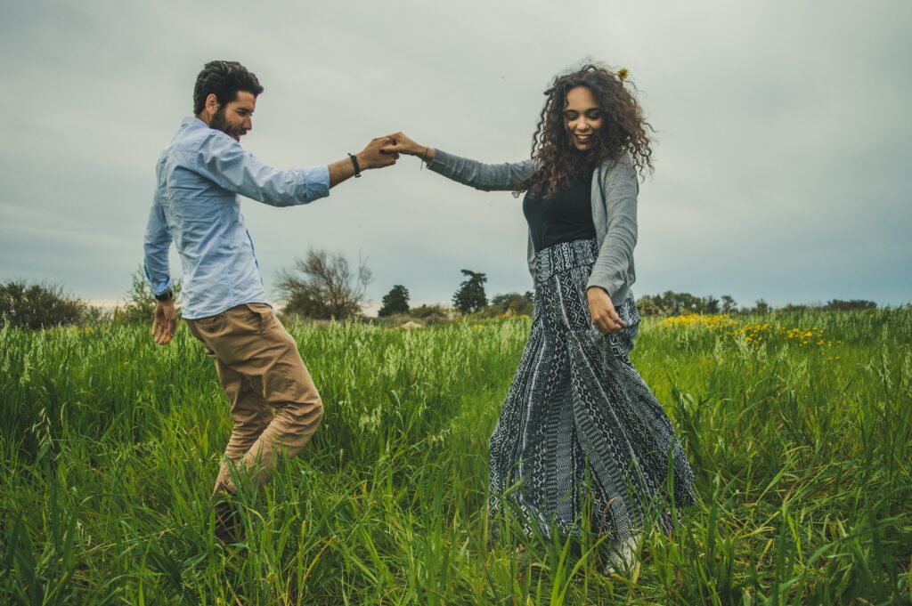 This enchanting image captures a couple dancing gracefully in a field of lush green grass. Their joy is palpable as they move harmoniously, surrounded by nature's vibrant hues. The scene exudes happiness, love, and the carefree beauty of shared moments in the great outdoors as they are elevating relationships through self-care.