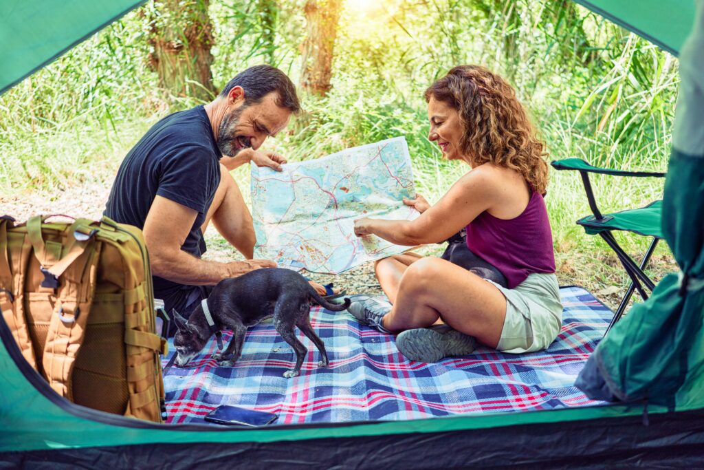 Image of a couple in the wilderness, this adventurous couple shares smiles as they navigate their camping trip with the help of a trusty map, accompanied by their faithful canine companion. Surrounded by the enchanting beauty of the woods, they embrace the 5 Ways to Support Mental Health in Relationships